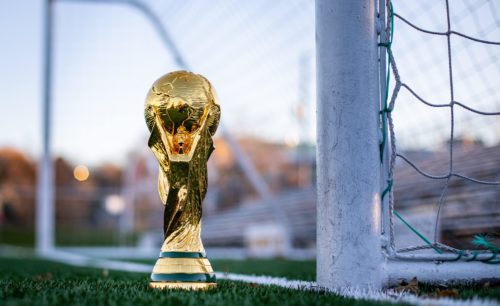 World Cup trophy close to the goal net on the field - Why The World Cup is Held Every 4 Years - thegamerian.com