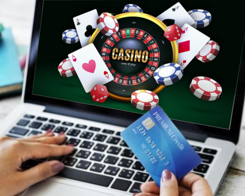 Unknown hand holding a payment card in front of a laptop with casino background - How to Play Casino Games - thegamerian.com Gaming Blog 
